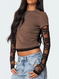 Woman wearing a brown crop top with lace sleeves and jeans on a light gray background
