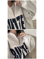A light heather gray zip-up hoodie with a large navy blue graphic text print on the front, shown in a two-panel close-up on a model.