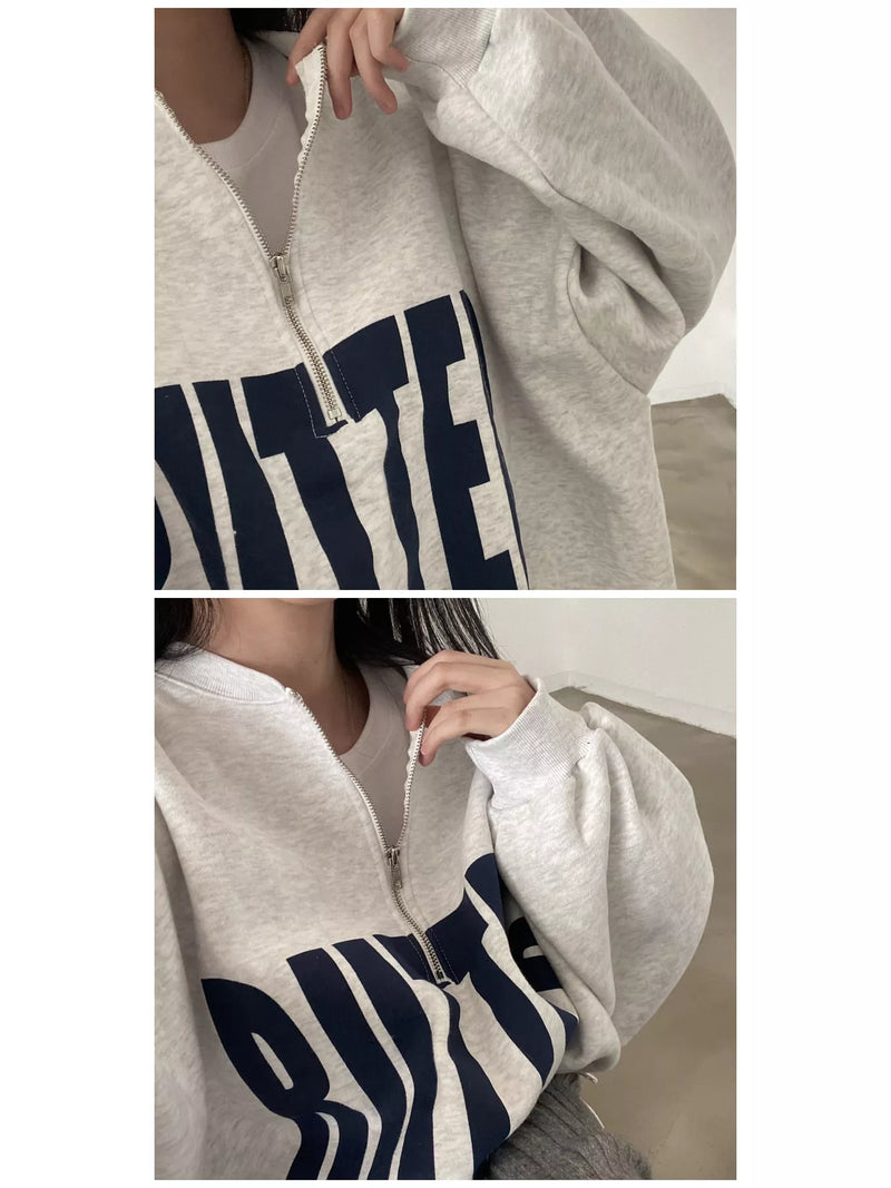 A light heather gray zip-up hoodie with a large navy blue graphic text print on the front, shown in a two-panel close-up on a model.