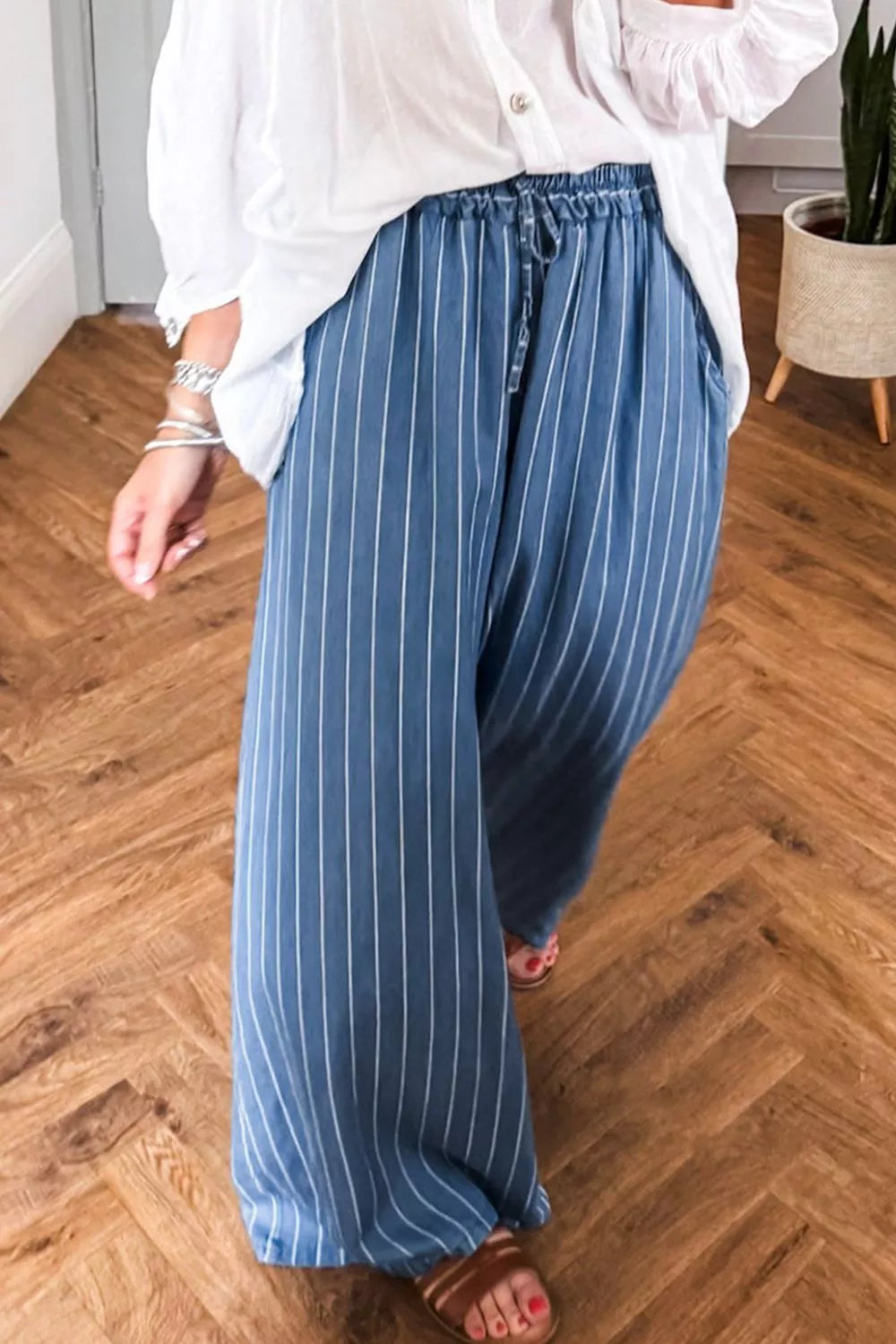 Person wearing blue striped pants and a white shirt on a wooden floor.