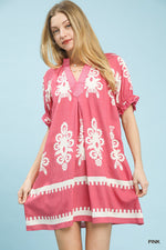 Woman wearing a pink dress with white patterns on a light blue background