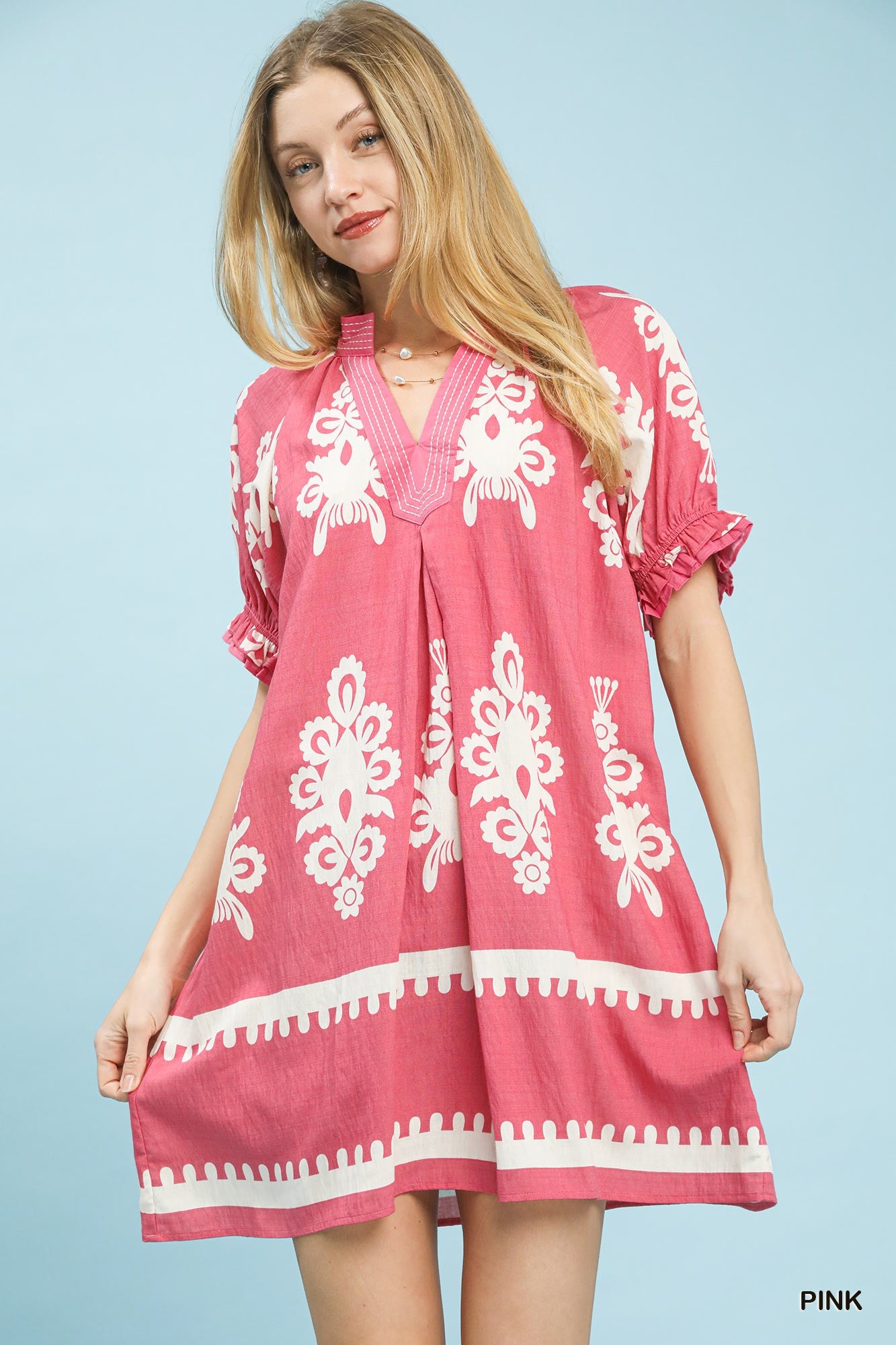 Woman wearing a pink dress with white patterns on a light blue background