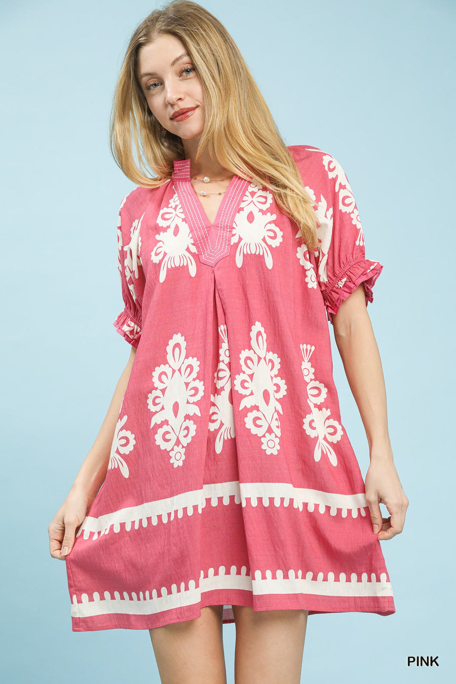 Woman wearing a pink dress with white patterns on a light blue background