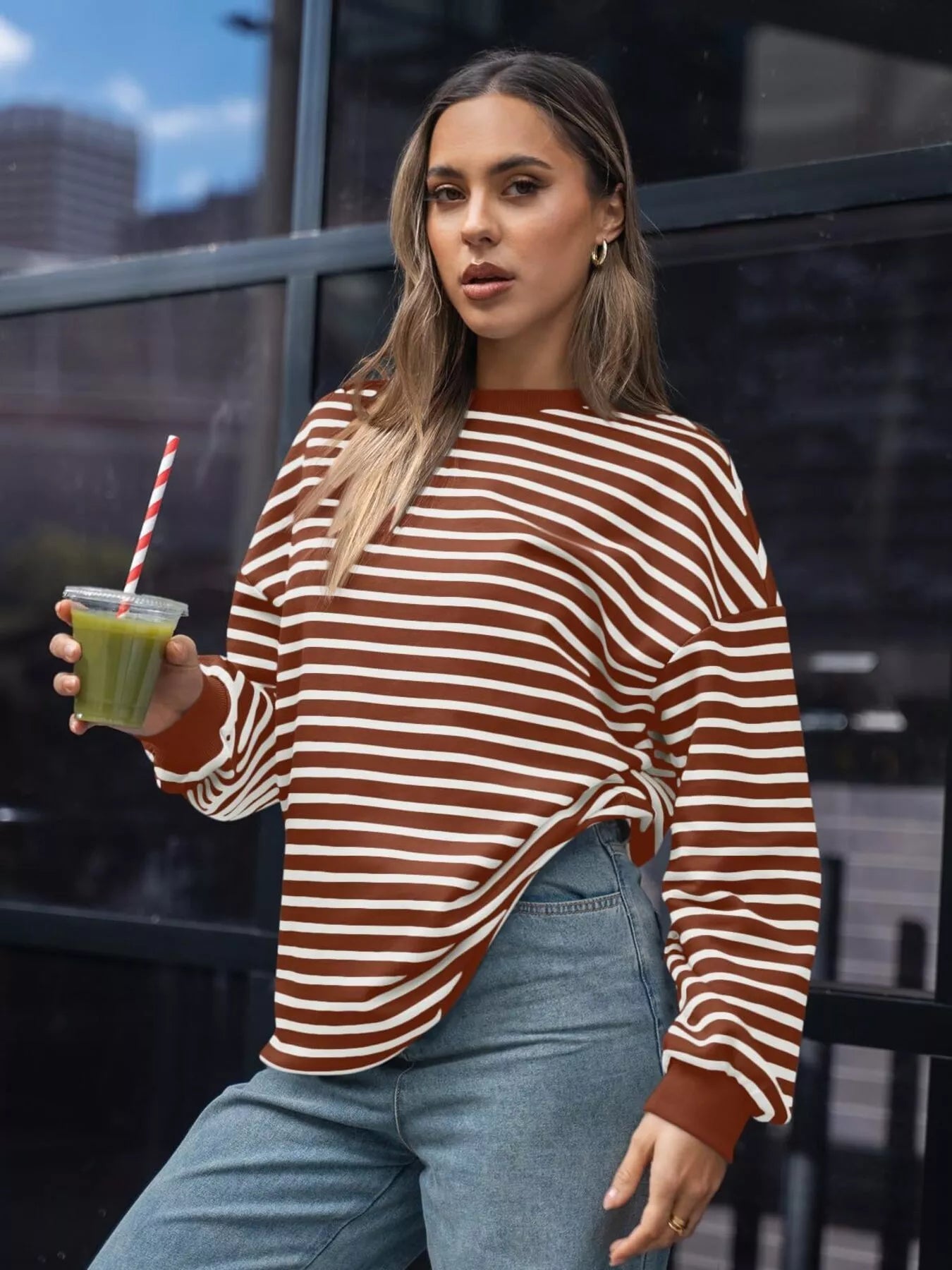 Woman in a striped sweater holding a green smoothie in an urban setting