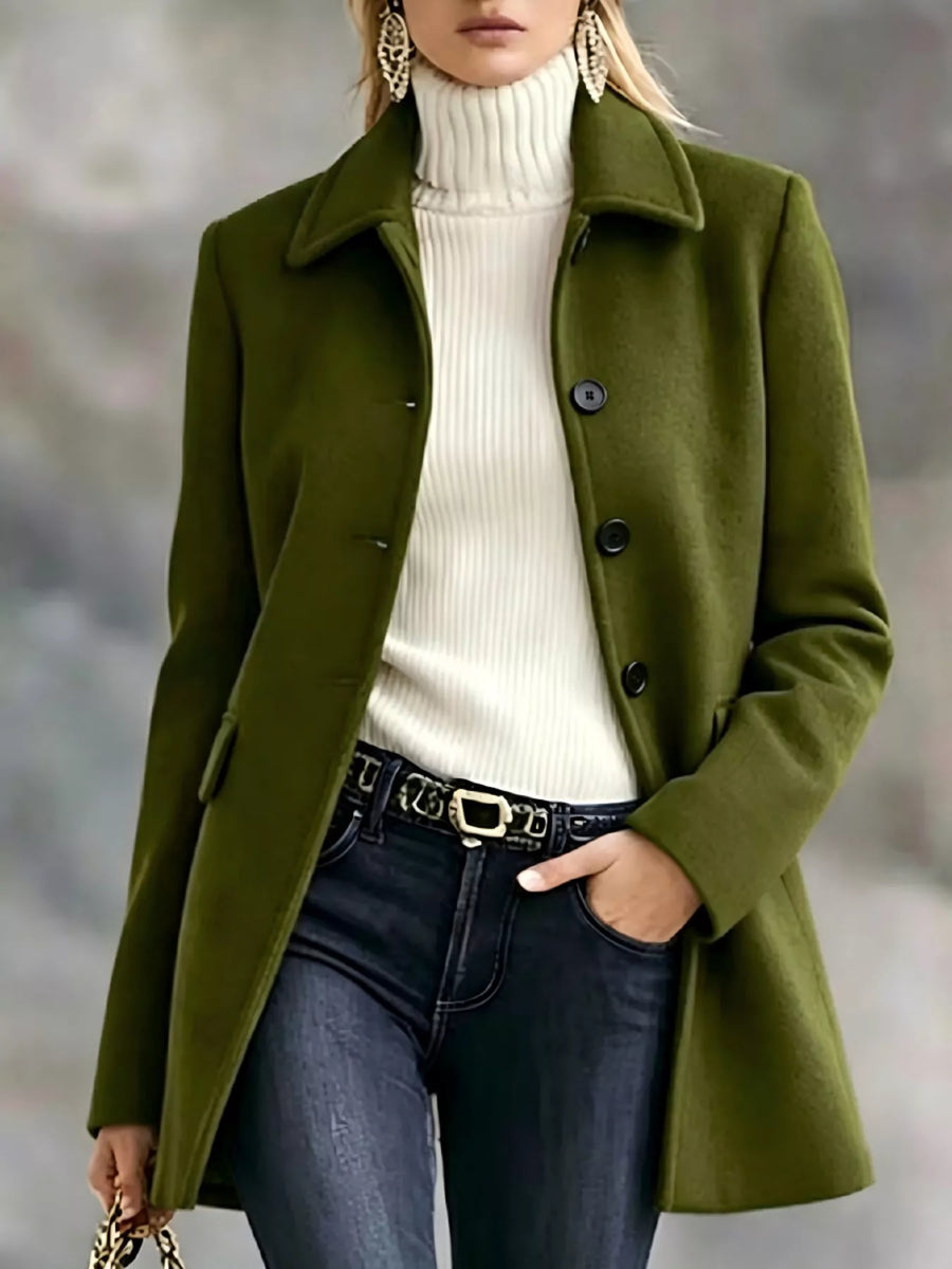 A woman wearing an olive green wool-blend coat over a cream ribbed turtleneck sweater, paired with dark blue jeans and a black belt with a gold buckle.