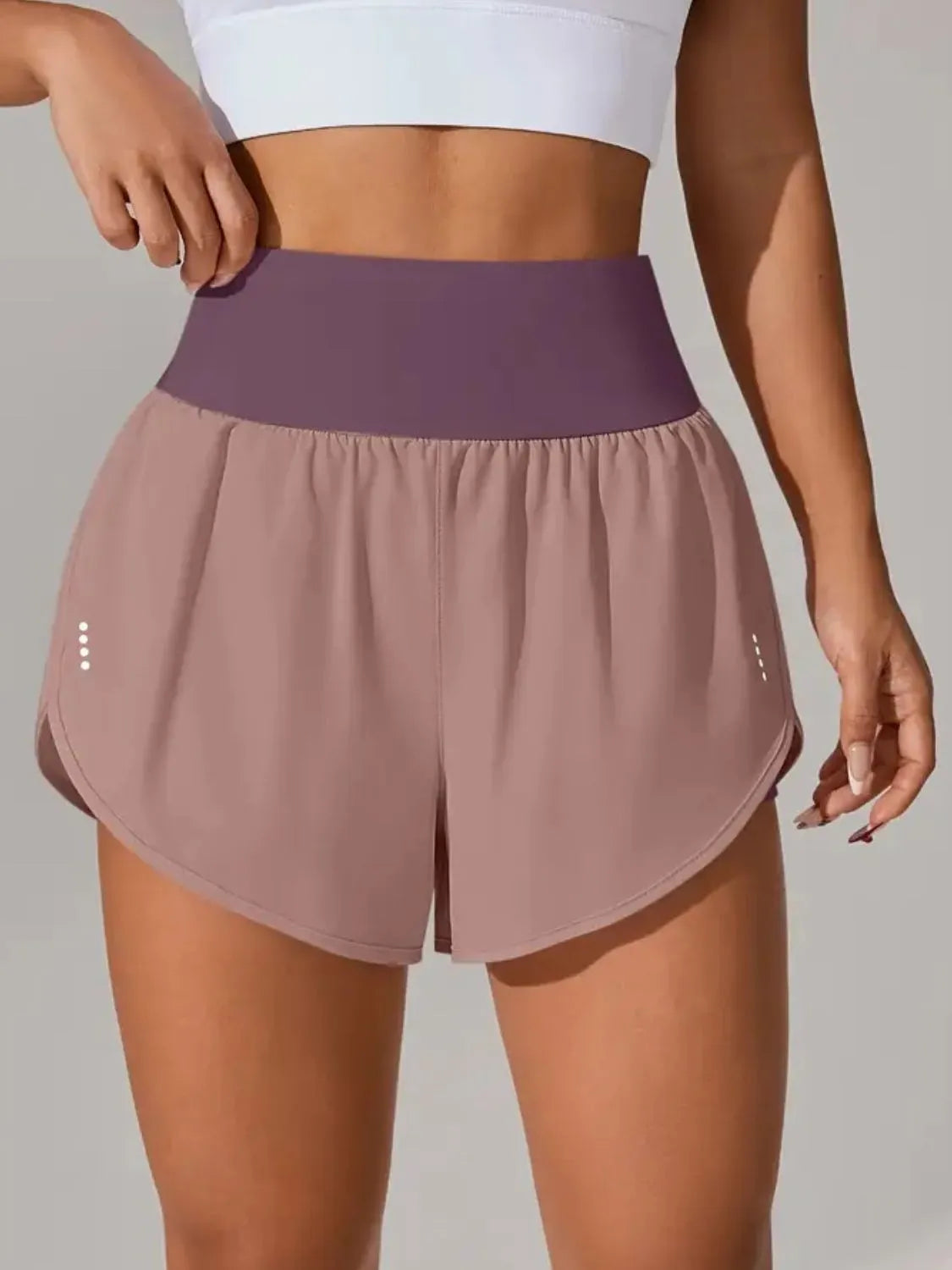 Person wearing mauve athletic shorts with a purple waistband on a neutral background