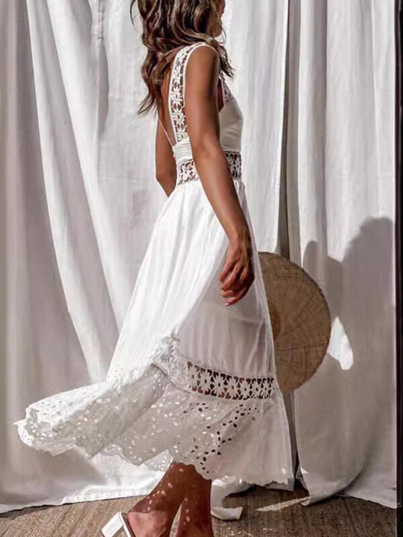Woman wearing a white dress with lace details standing in front of sheer curtains.