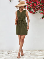Woman wearing a green dress and straw hat standing against a white wall with red flowers.