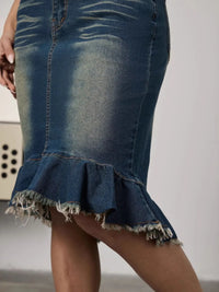 Close-up of a blue denim skirt with ruffled hem on a plain background