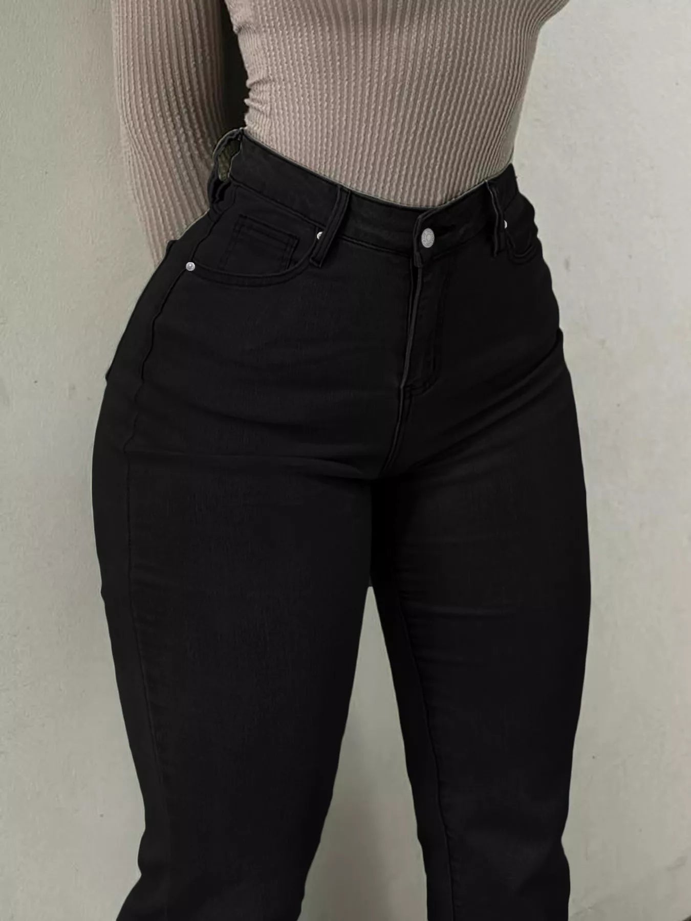 Person wearing black pants and a beige top against a plain background