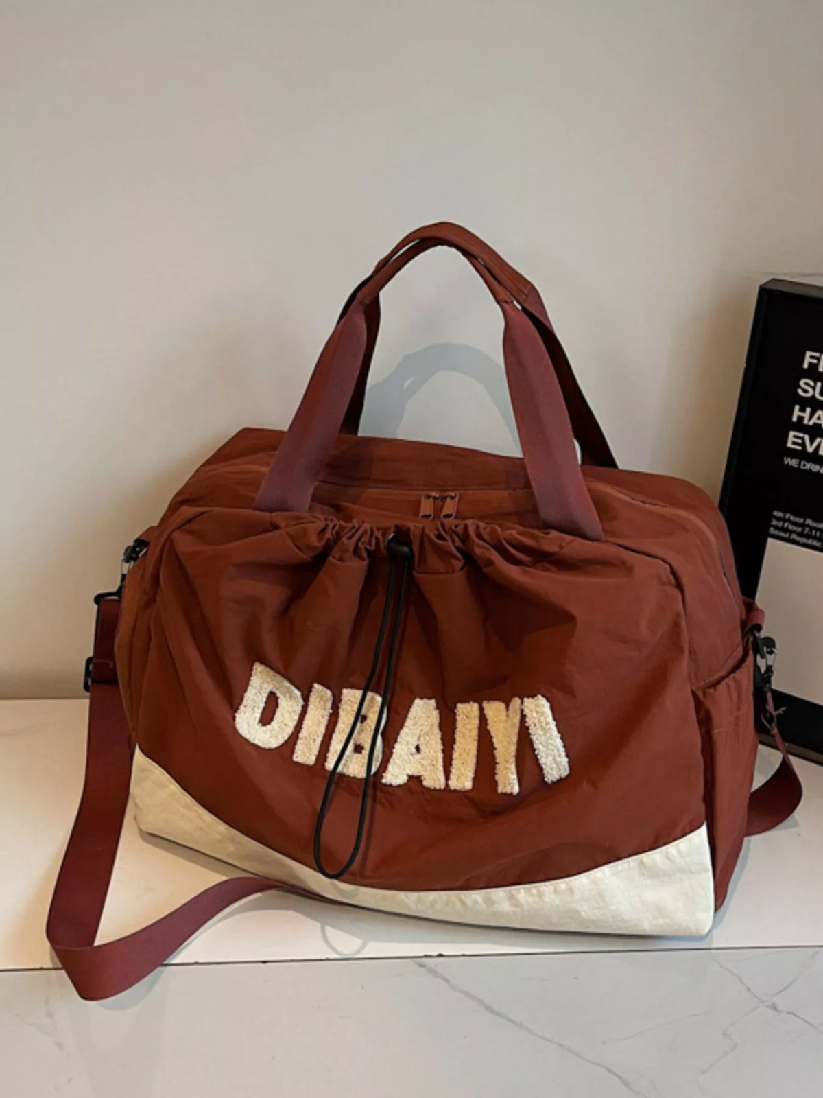 Brown duffel bag with 'Dubai' text on a white surface