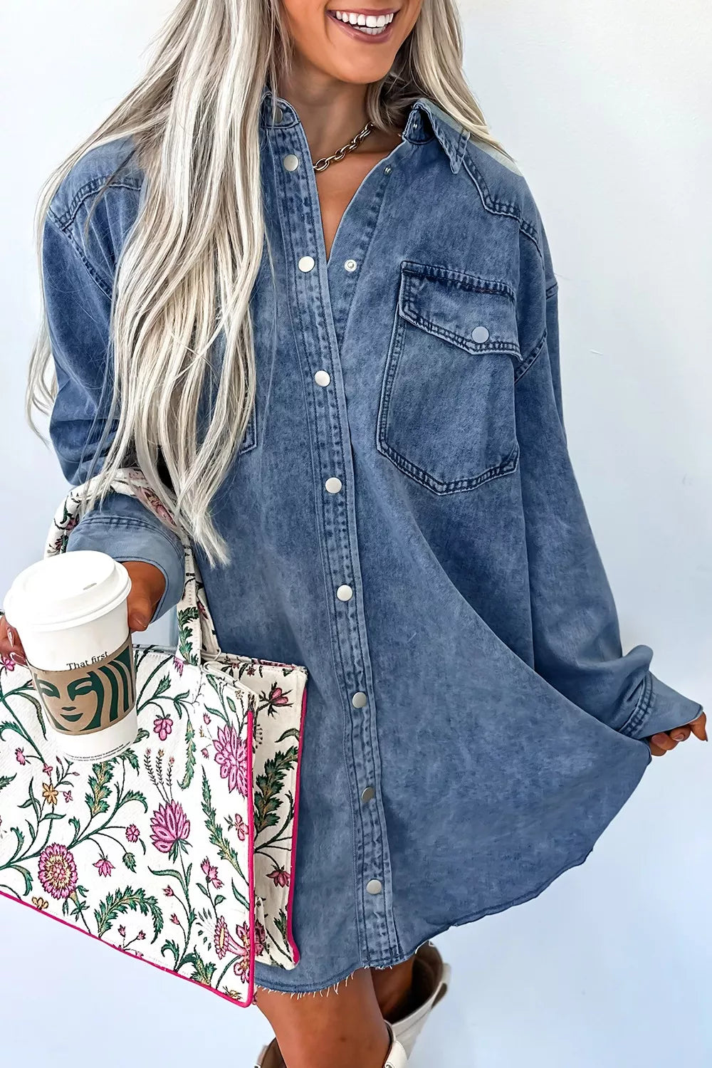Woman wearing a denim dress holding a floral bag against a white background