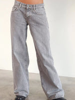 A person wearing light gray wide-leg denim jeans, shown from the waist down against a plain off-white wall and concrete floor.