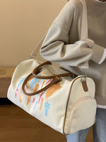 Beige duffel bag with colorful designs held by a person wearing a beige sweatshirt.