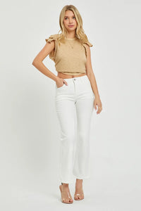 Woman wearing a beige top and white pants on a plain background