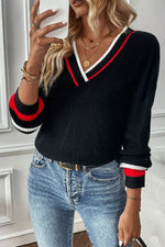 Person wearing a black sweater with red and white trim and blue jeans indoors.