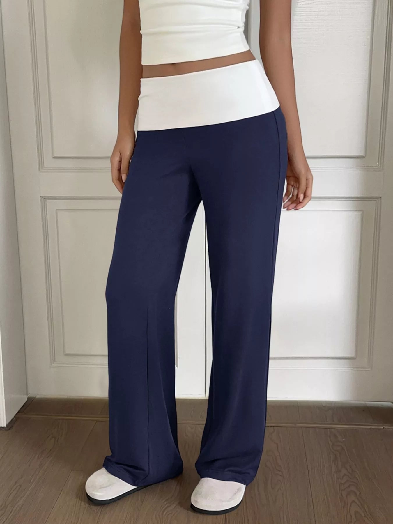 Person wearing navy pants and a white top against a neutral background