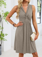 Woman wearing a gray dress holding a clutch in a bright room with plants.