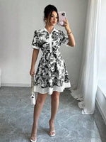 Woman taking a mirror selfie wearing a black and white floral dress in a room with white walls and curtains.