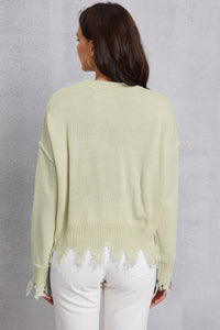 Person wearing a light green sweater with distressed hem against a gray background