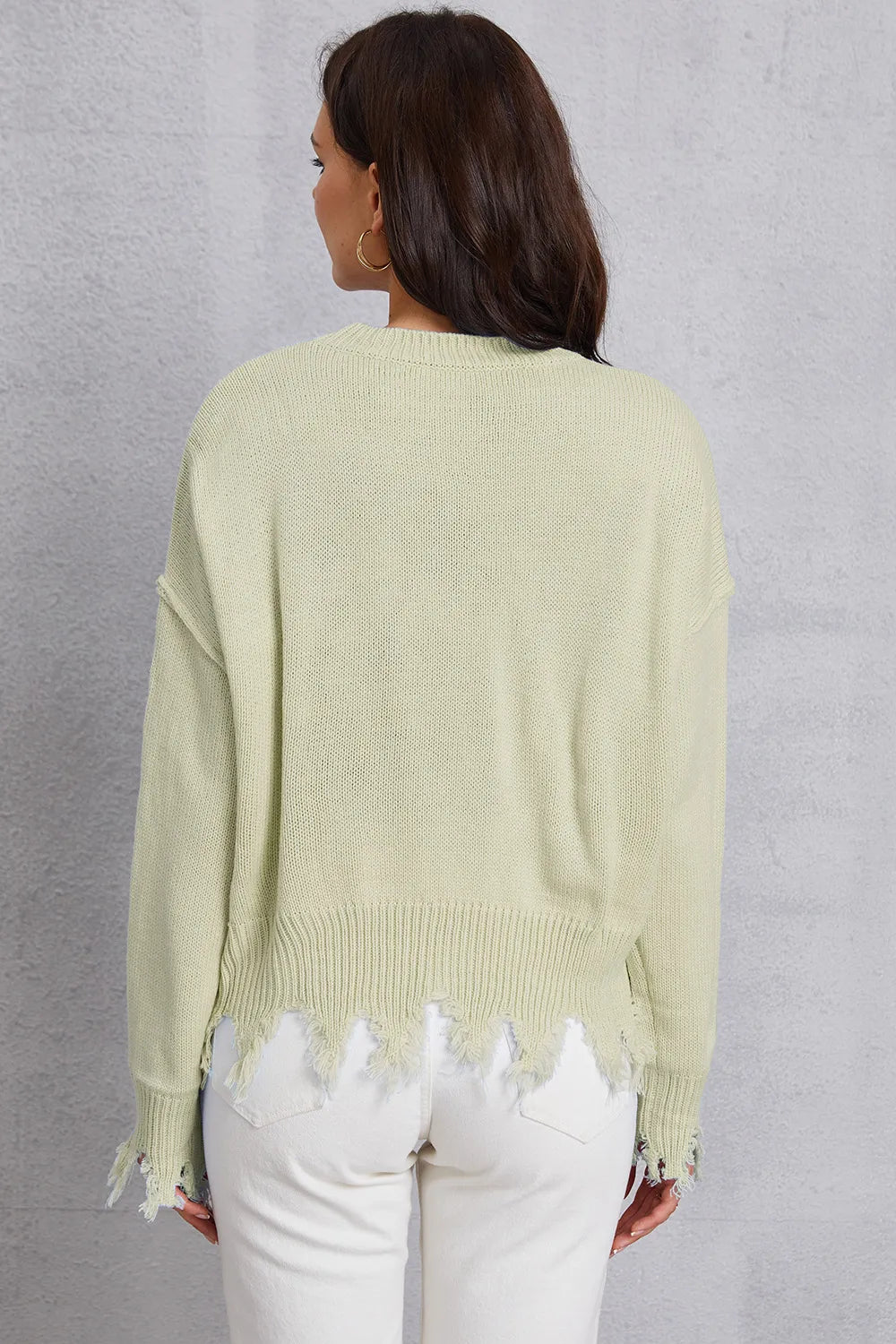 Person wearing a light green sweater with distressed hem against a gray background