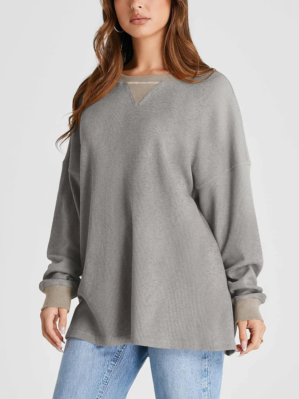 Woman wearing a gray oversized sweater and blue jeans on a light gray background