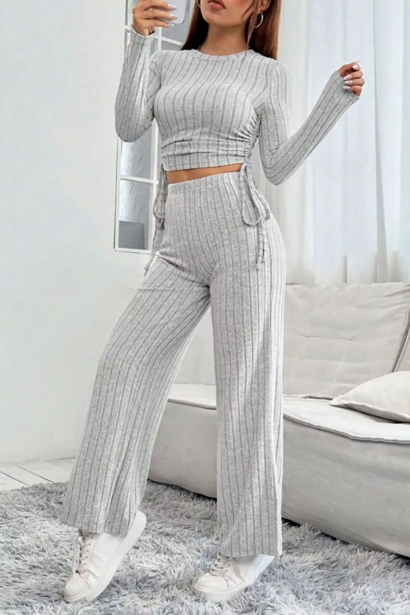 Woman wearing a gray ribbed outfit with long sleeves and pants in a minimalistic room.