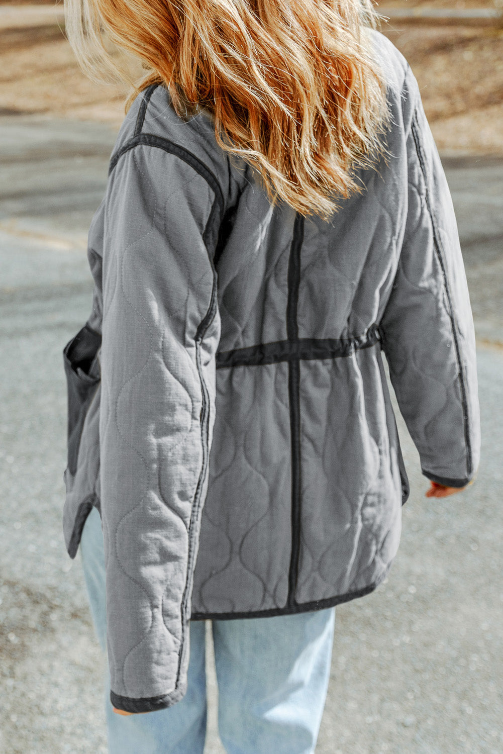 Person wearing a gray quilted jacket with a neutral background