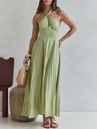 Woman wearing a light green halter neck dress holding a woven bag against a neutral background