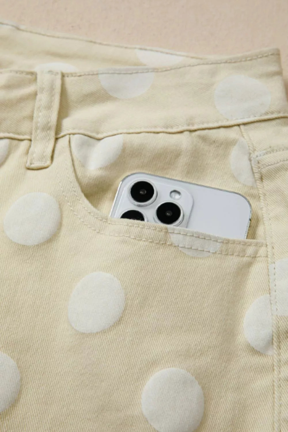 Phone in a pocket of beige pants with white polka dots