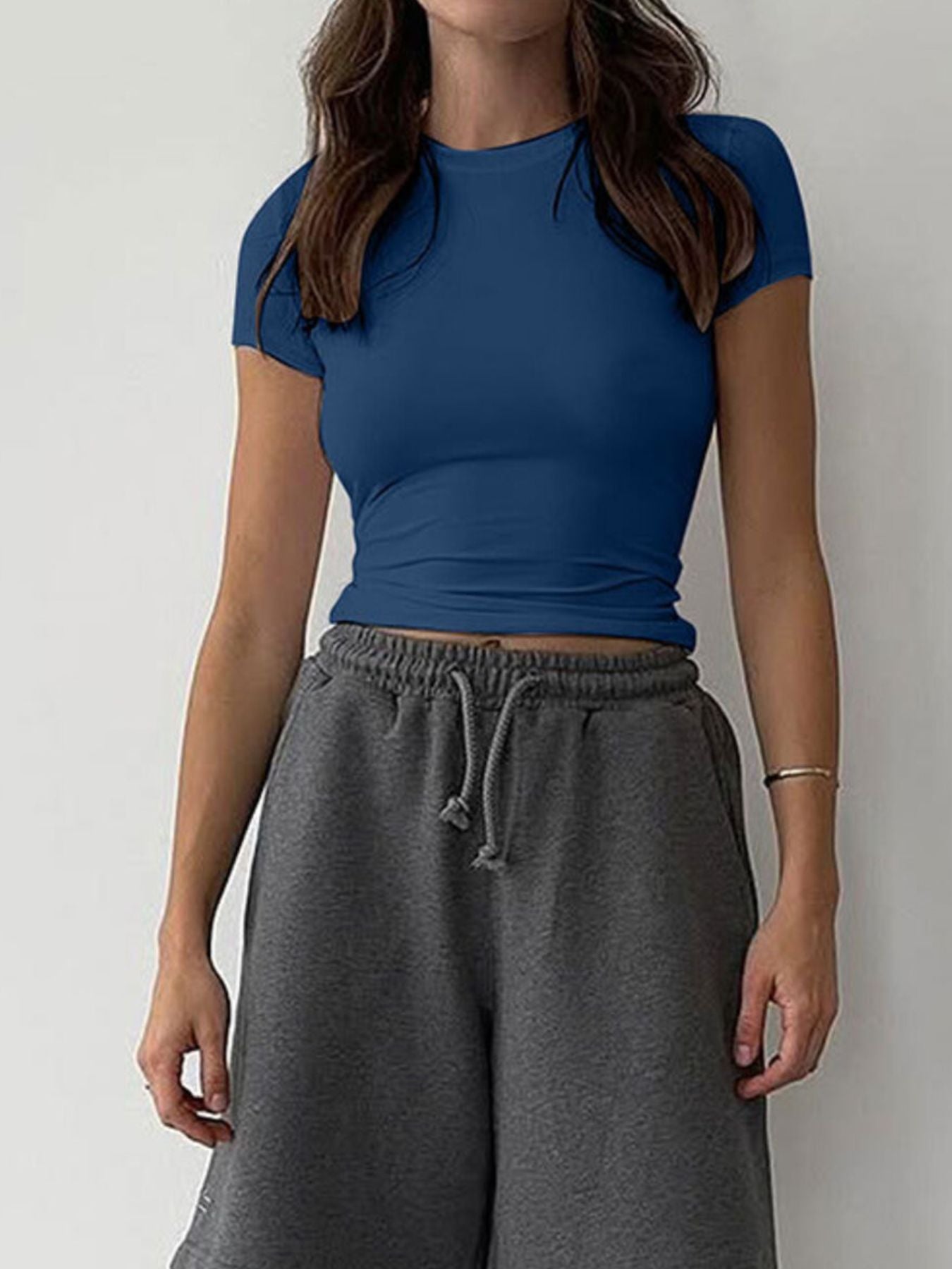 Person wearing a blue crop top and gray sweatpants against a plain background