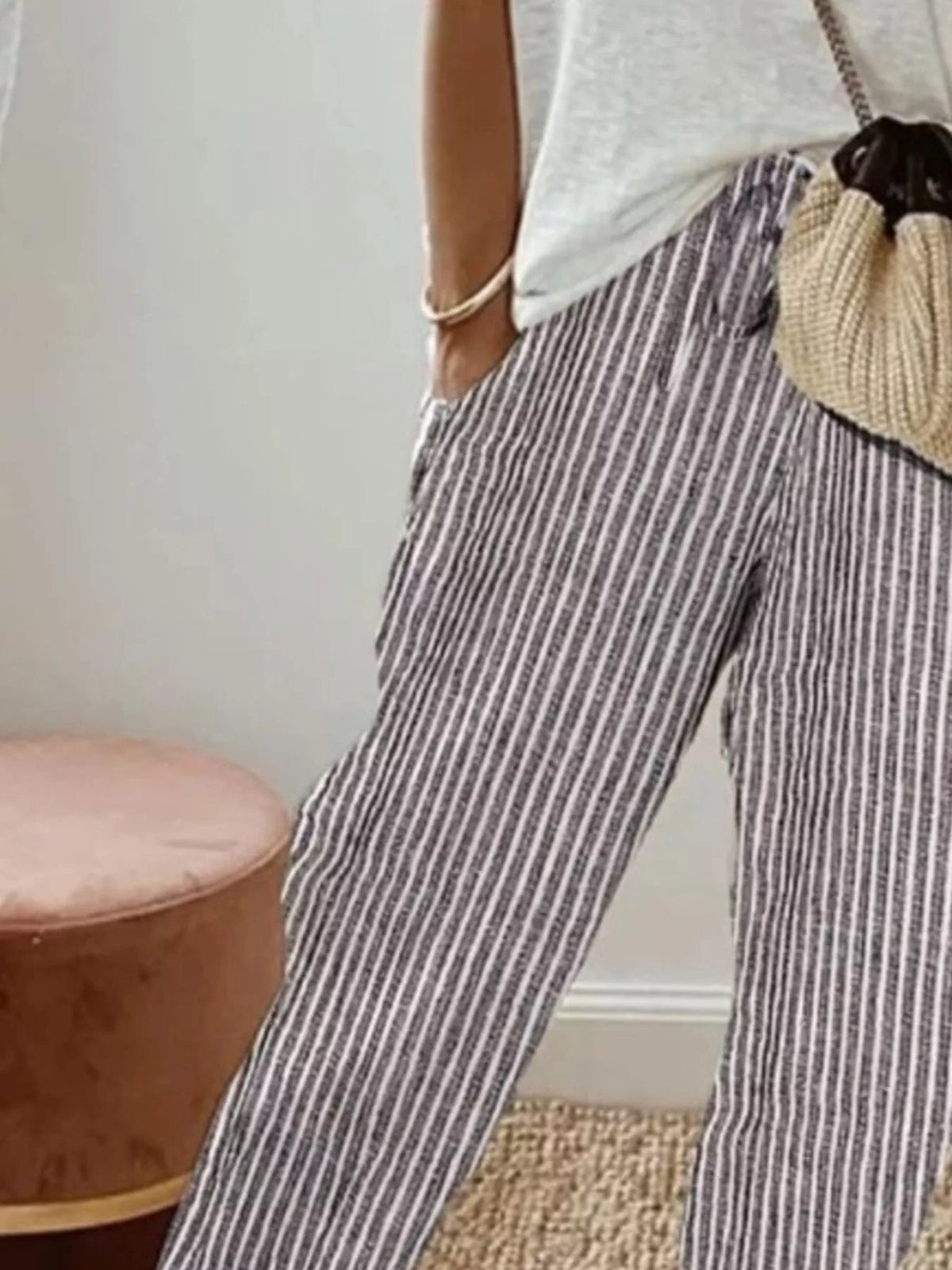 Person wearing striped pants with a neutral-colored bag in a minimal indoor setting