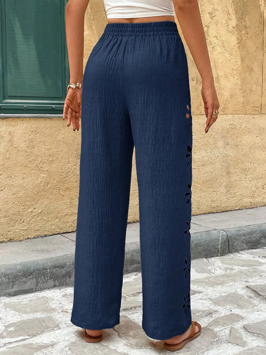 Person wearing navy blue pants standing on a street with a beige wall in the background