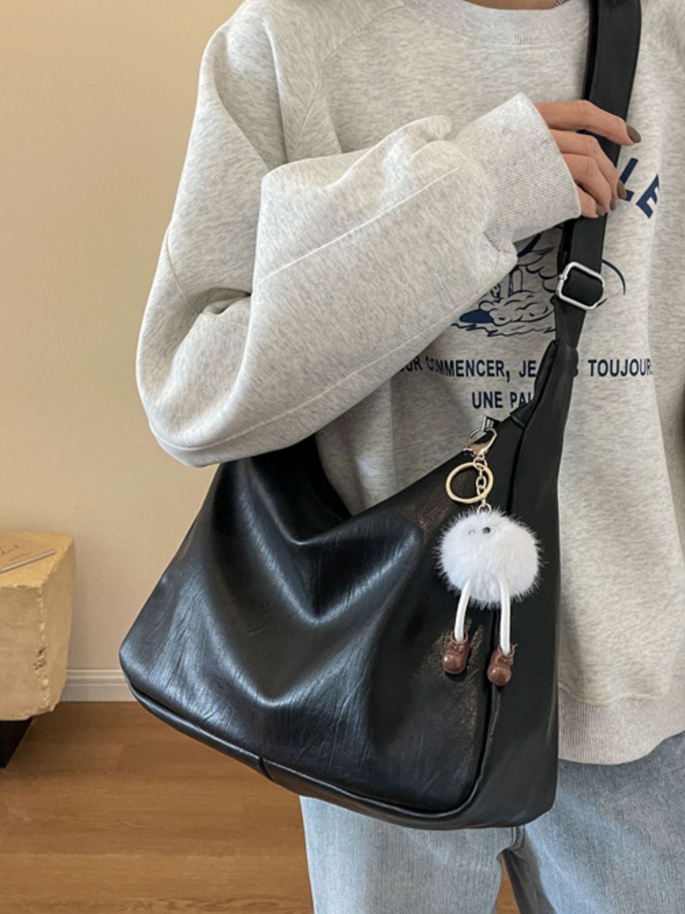 Person holding a black handbag with a fluffy white keychain, wearing a light gray sweatshirt.