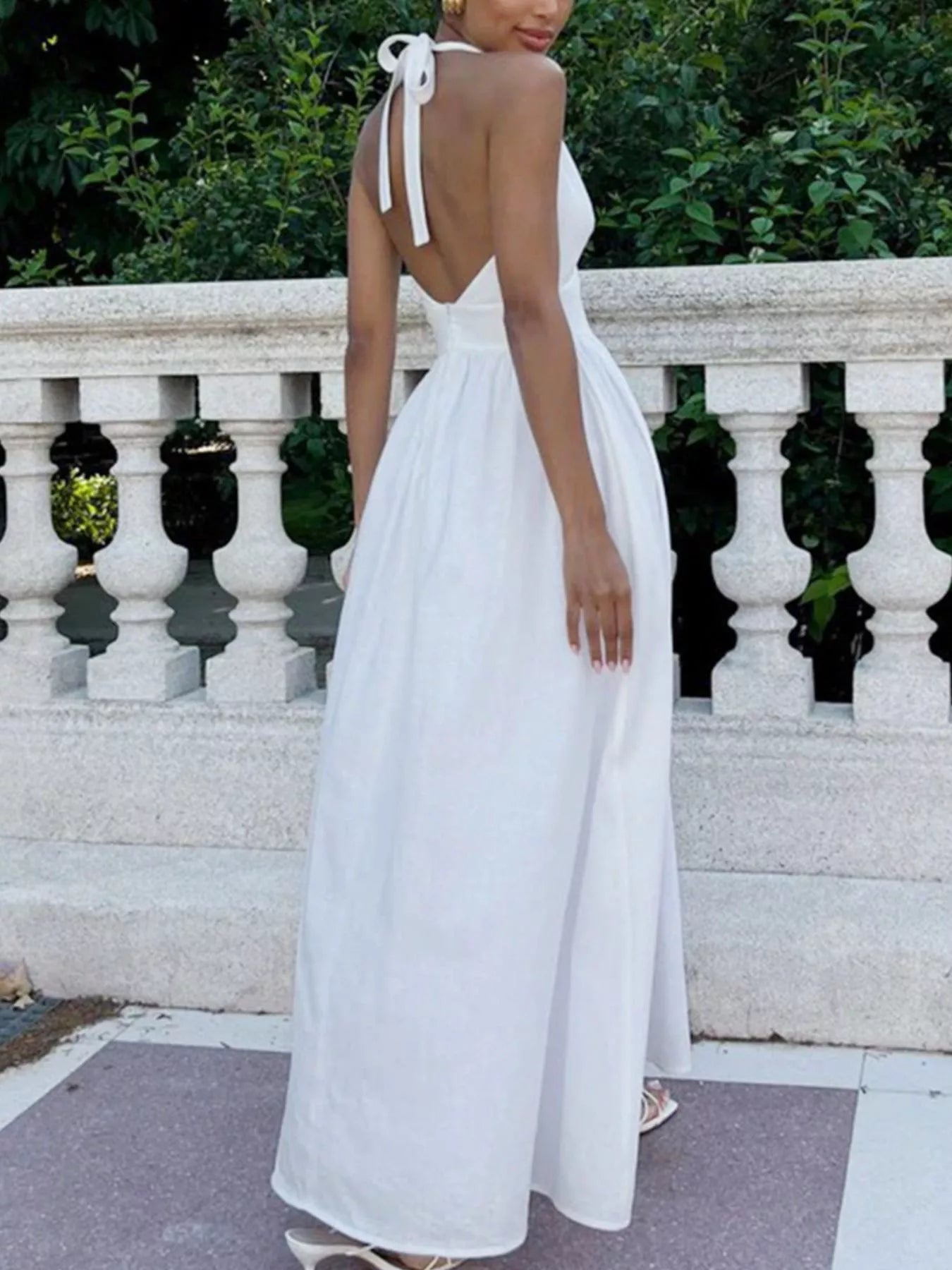 Woman wearing a white dress with a backless design, standing outdoors.
