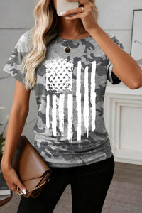 Person wearing a gray camouflage t-shirt with an American flag design, holding a phone.