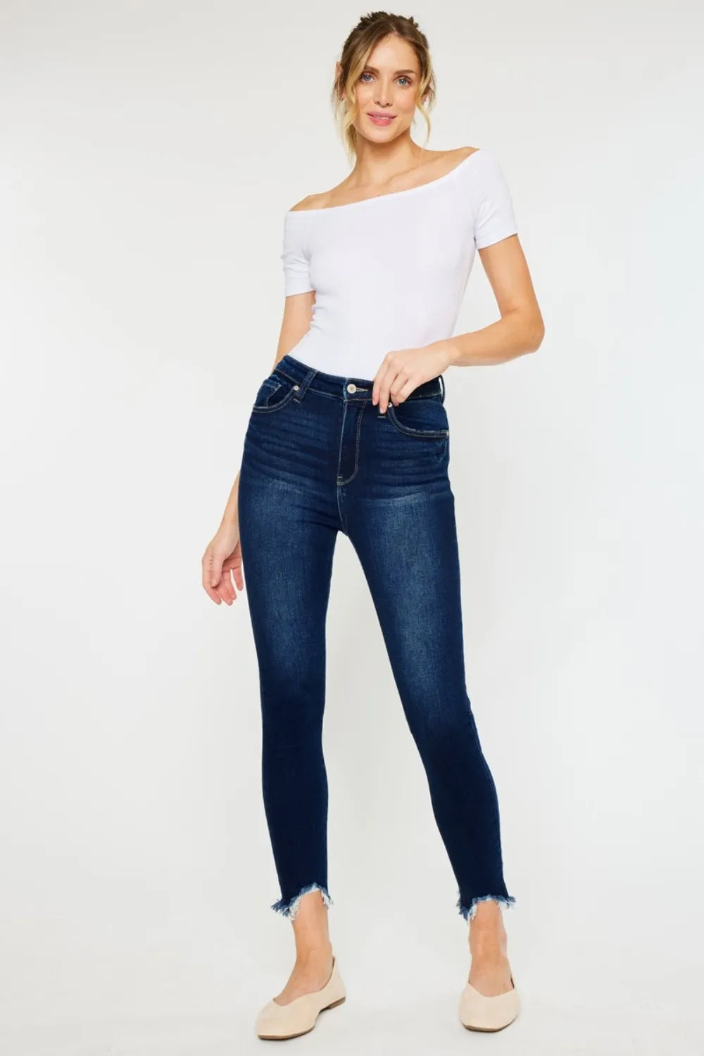Woman wearing a white off-shoulder top and dark blue jeans on a white background