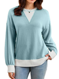 Woman wearing a light blue ribbed sweater with a white shirt underneath on a white background