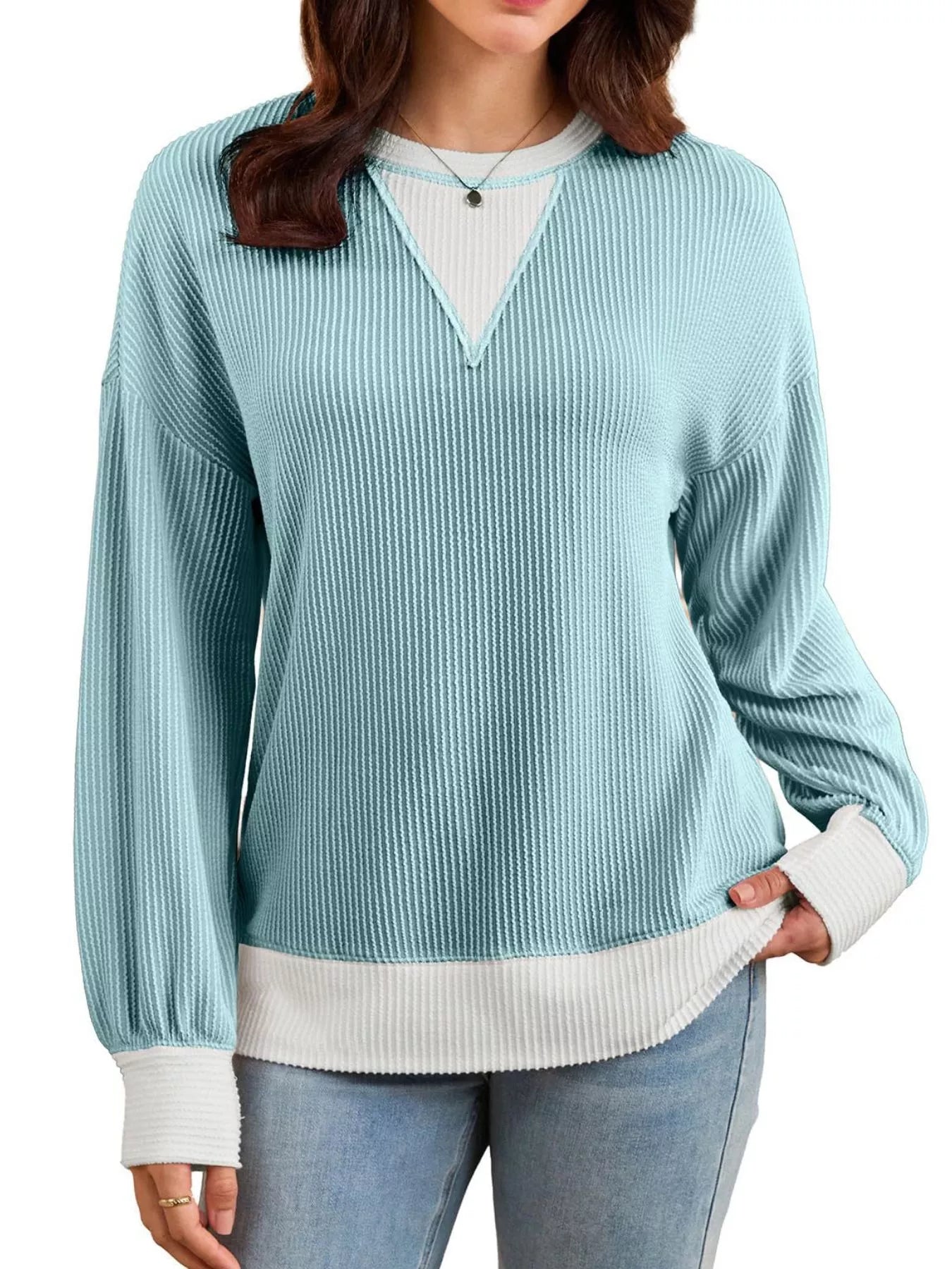 Woman wearing a light blue ribbed sweater with a white shirt underneath on a white background