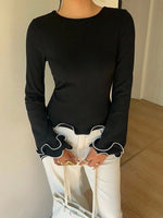 Person wearing a black long-sleeve top with white cuffs and trim, paired with white pants.