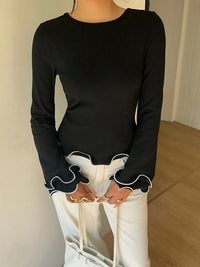 Person wearing a black long-sleeve top with white cuffs and trim, paired with white pants.
