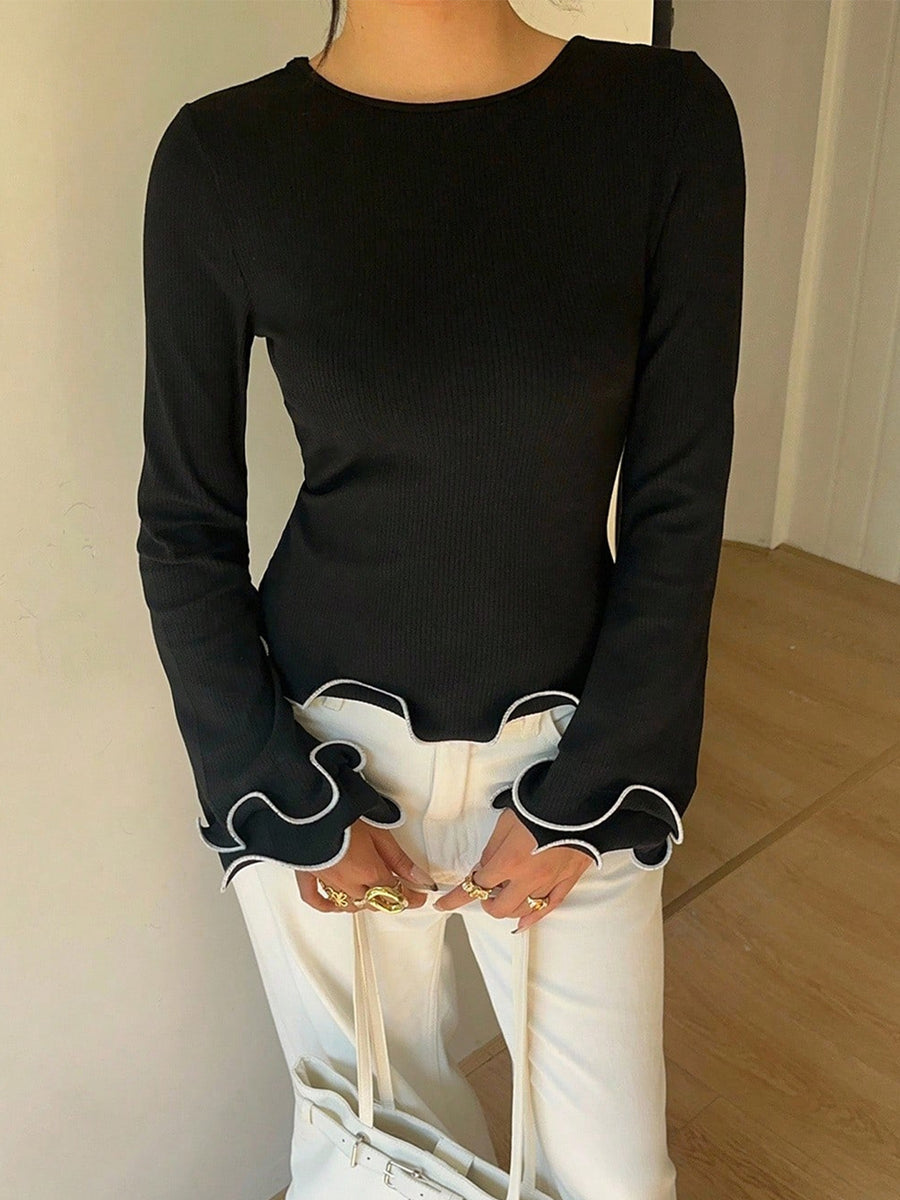 Person wearing a black long-sleeve top with white cuffs and trim, paired with white pants.