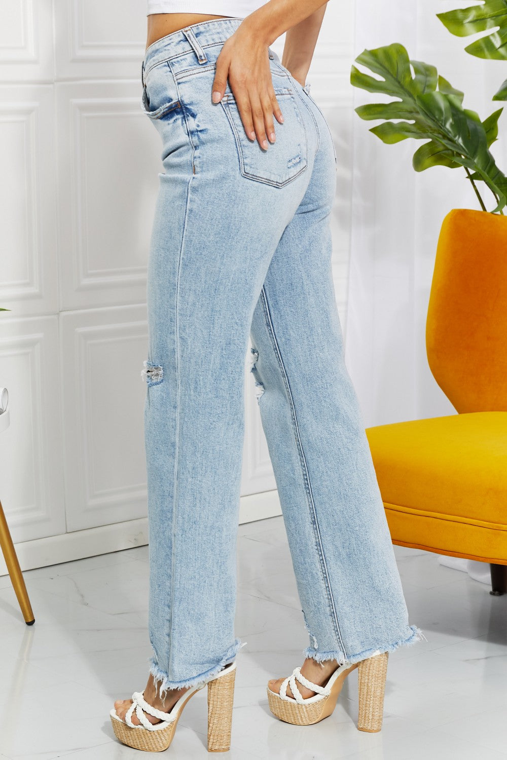 Person wearing light blue jeans with a white wall and orange chair in the background