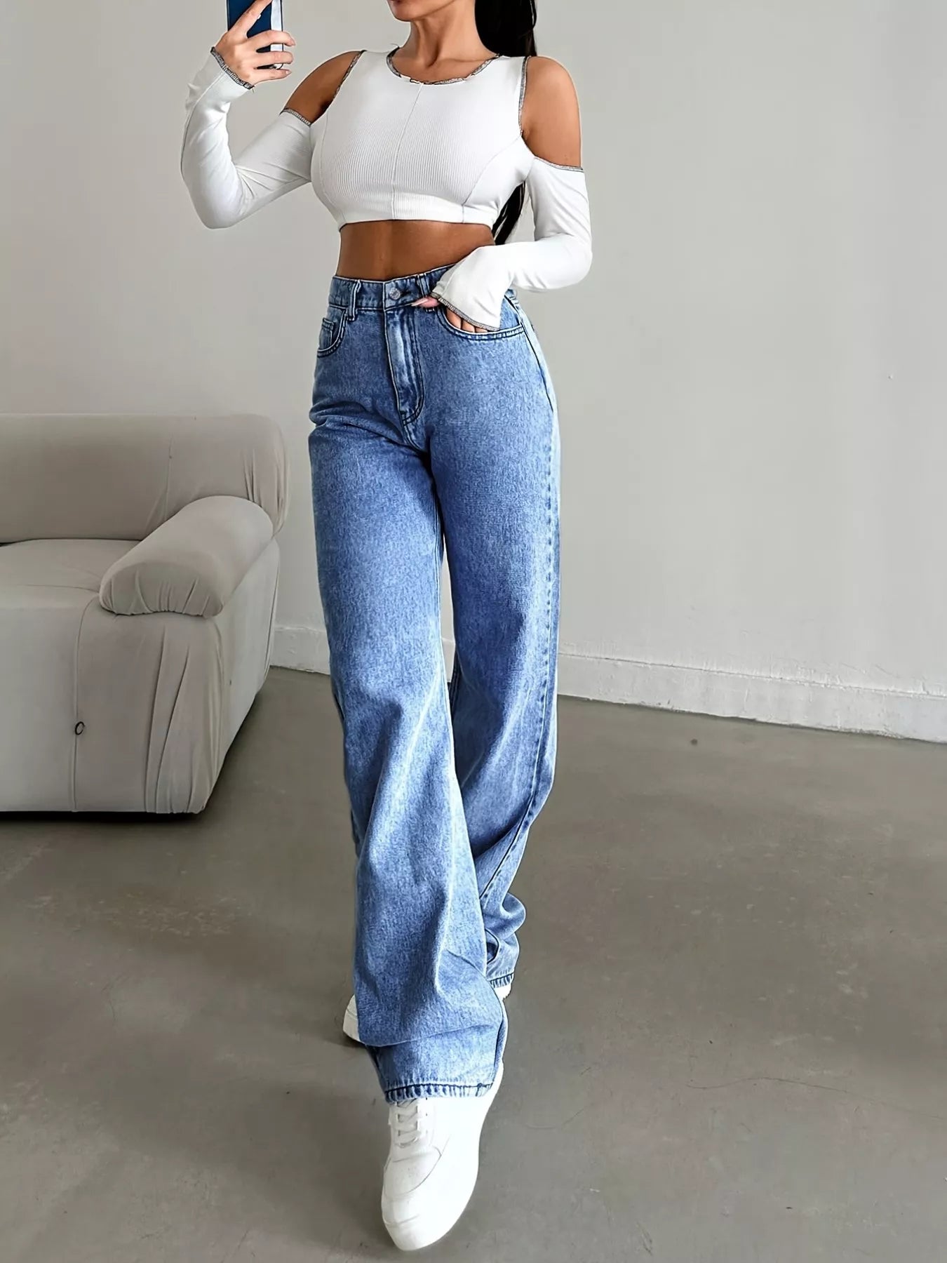 Person wearing a white crop top and blue jeans in a minimalistic room.