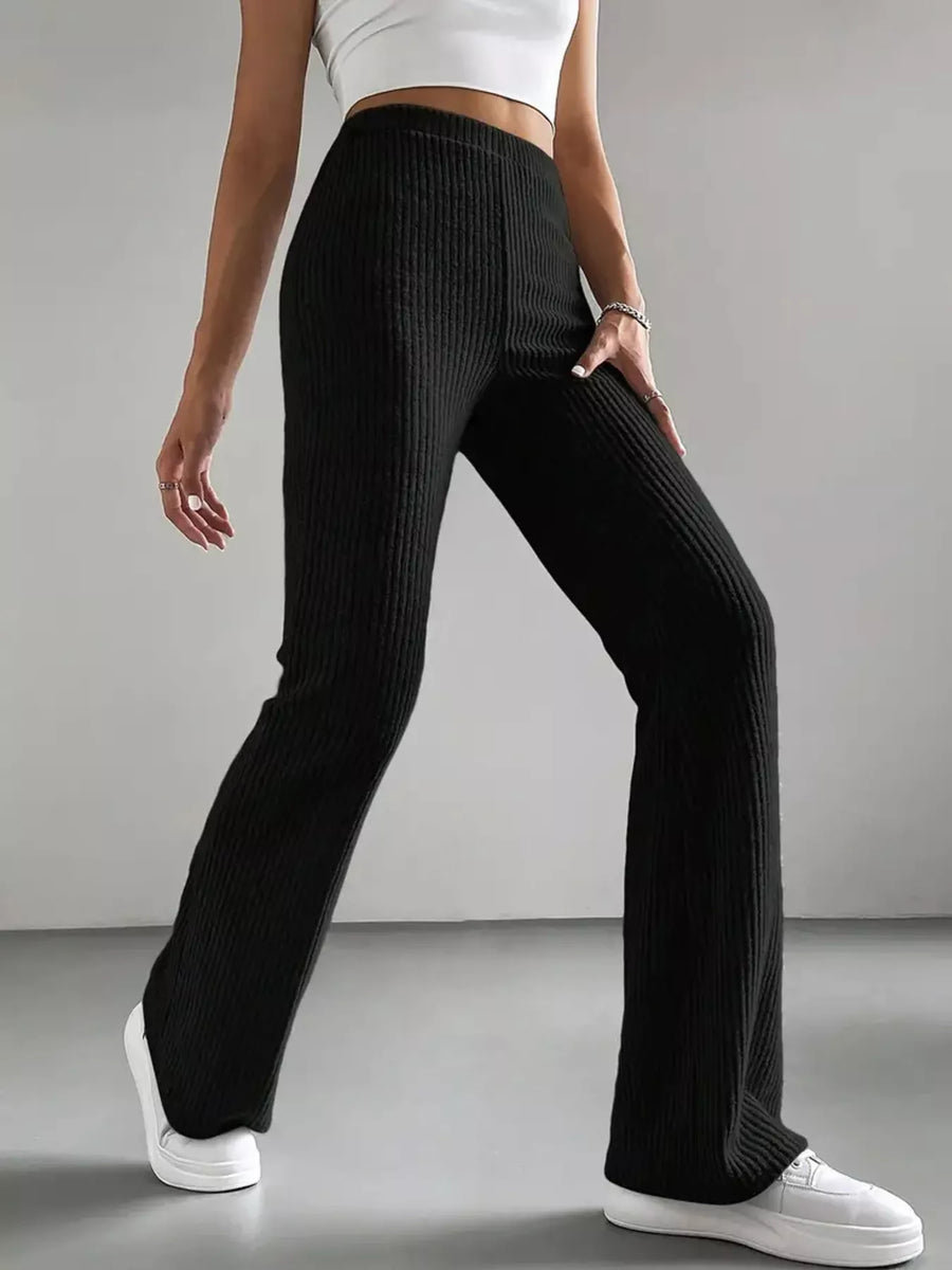 Person wearing black ribbed pants and white sneakers on a gray background