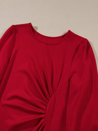 Red long-sleeve top with a knot detail on a beige background