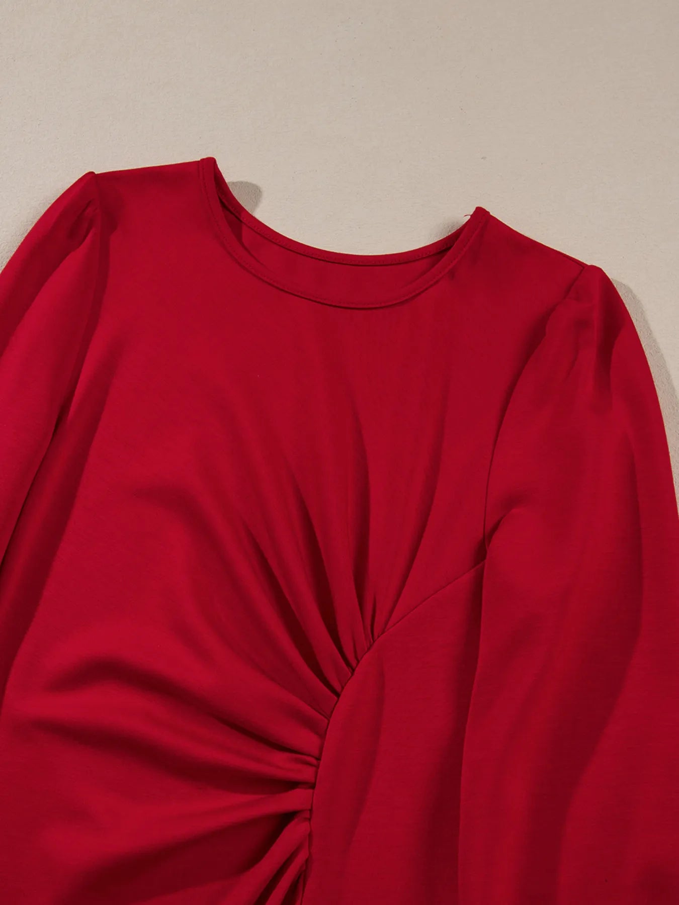 Red long-sleeve top with a knot detail on a beige background
