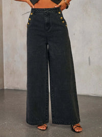 Black wide-leg jeans with gold buttons worn by a person against a neutral background