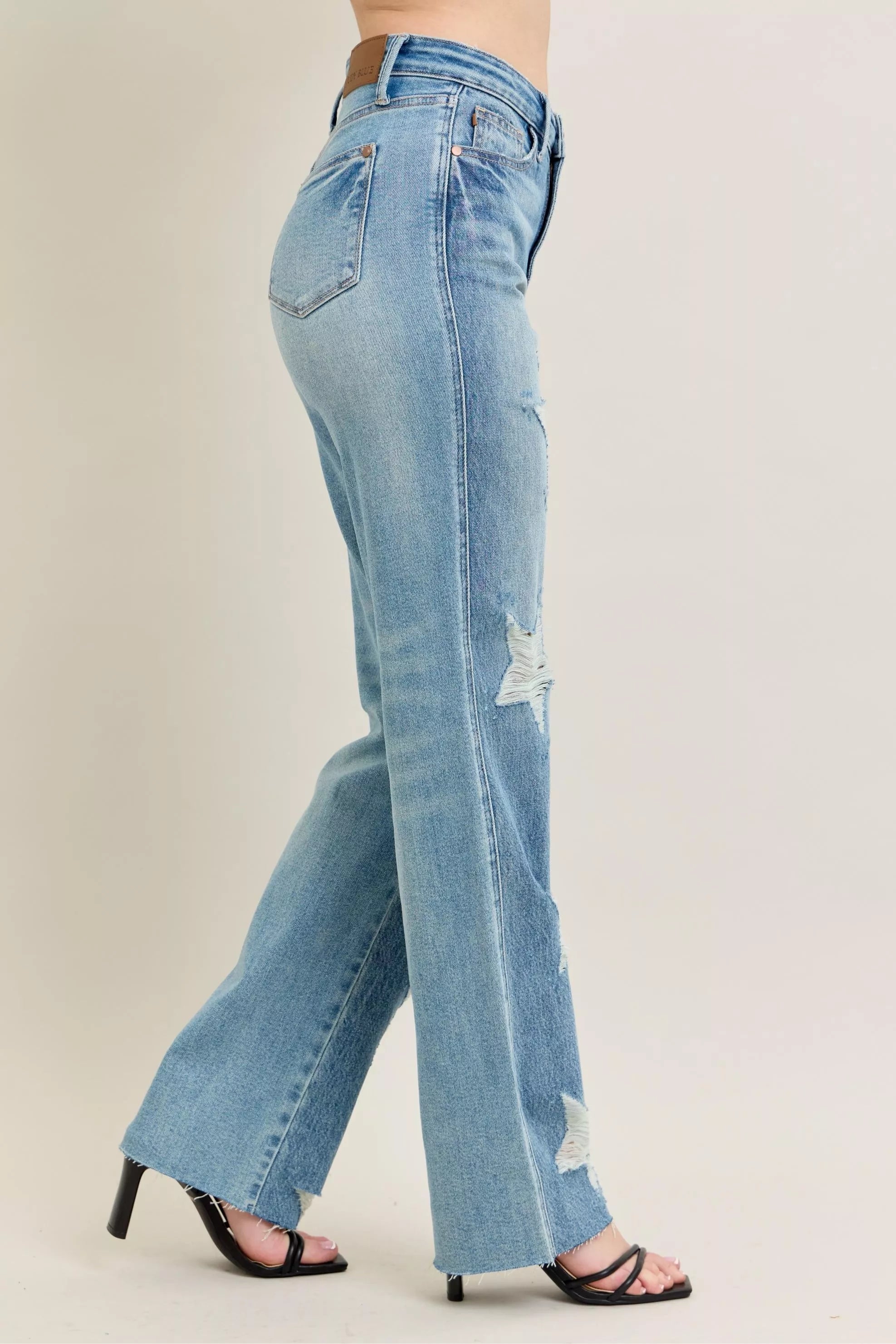 Light blue jeans with a slight distressed look worn by a person on a beige background