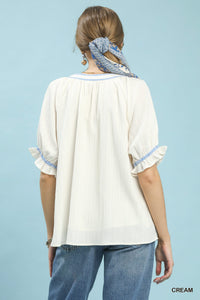 Woman wearing a cream blouse with blue trim against a light blue background
